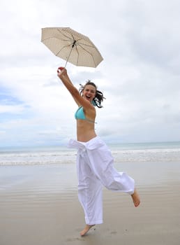 woman jumping on a tropical beach holding an umbrella 
