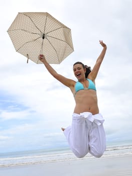 woman jumping on a tropical beach holding an umbrella 
