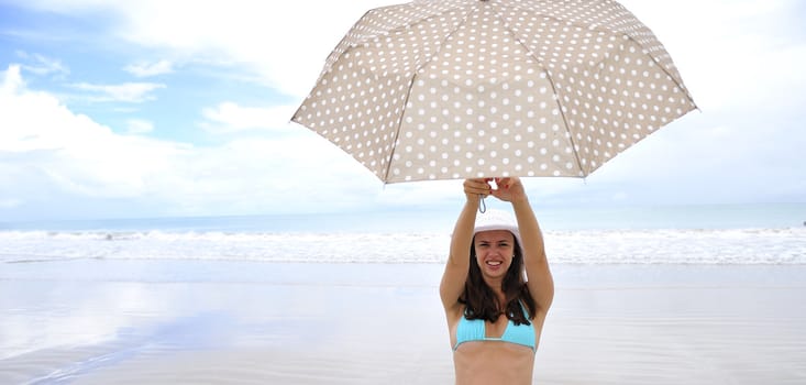 woman jumping on a tropical beach holding an umbrella 
