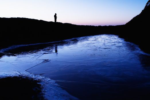 An iced lake with a man's silhouette in the morning.