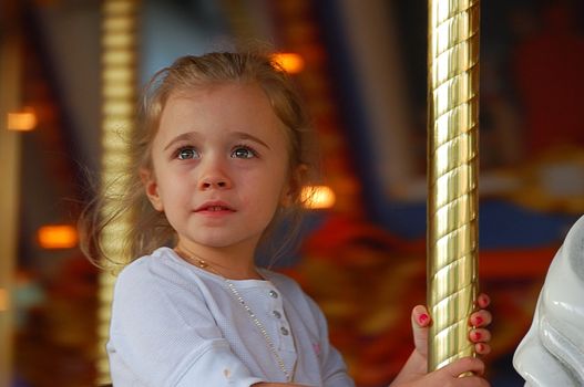 Little girl riding carousel with a look of wonderment