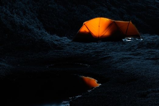 Tent in the night with weak light and small lake.