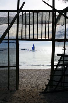 Fence on a beach and a drifting sailing boat on a sunset