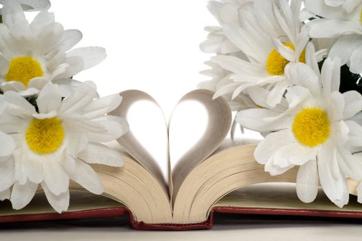 Closeup view of a romance novel with artificial flowers around the heart shaped pages