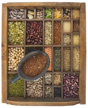 rustic scoop of red quinoa and a variety of beans, lentils, grain, seeds in old wooden typesetter case, isolated with clipping path, wide angle view showing box interior