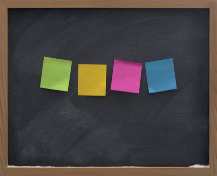 four blank, colorful (green, yellow, red, blue) sticky notes on blackboard with strong eraser smudge patterns