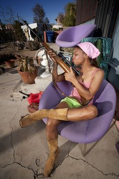 Black woman kissing rifle in front of house with messy yard