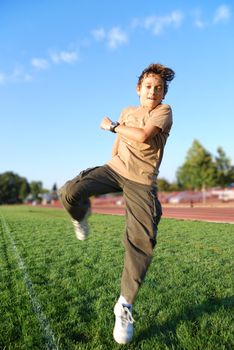 Teenage boy jumping in a green grass covered sports field on a sunny day.