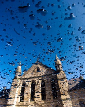 Church reflection on blue metallic surface with rain drops