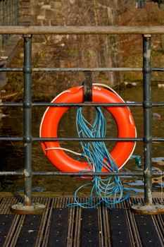 an orange old tatty life preserve secured to railings on a wooden river jetty.