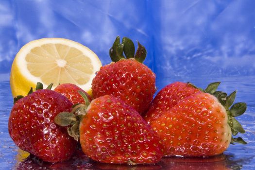 several wet strawberries and lemon with blue background