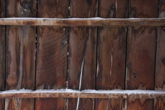 weathered wood of old barn wall with gaps between planks and snow