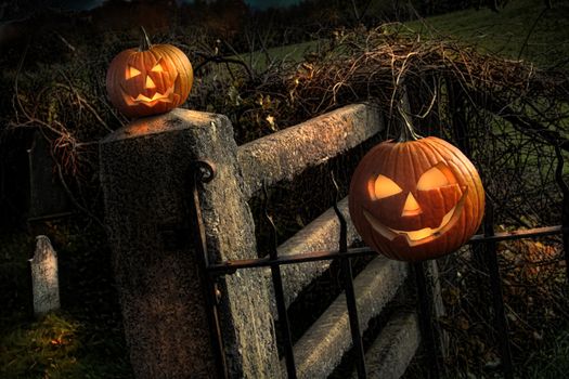 Two Halloween pumpkins sitting on a fence