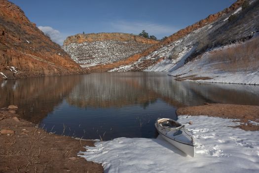 canoe and Colorado mountain lake (Horsetooth Reservoir near Fort Collins)  in early spring with red sandstone cliffs and snow