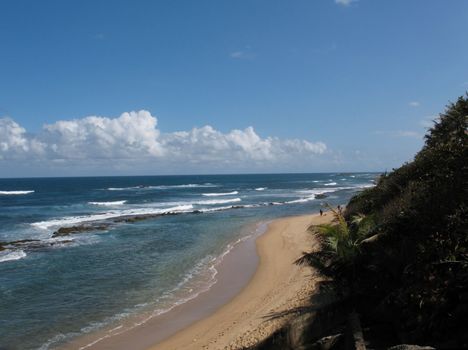 A view from San Juan, of the waves rolling in as a couple are walking the beach in the Eastern  Caibbean.