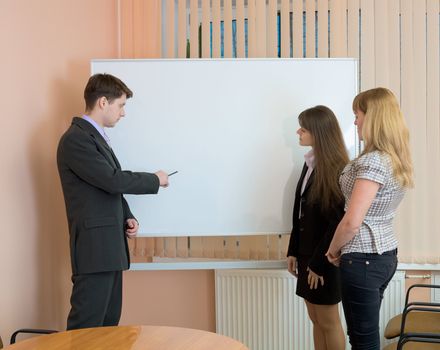 Office workers discuss work standing at a board