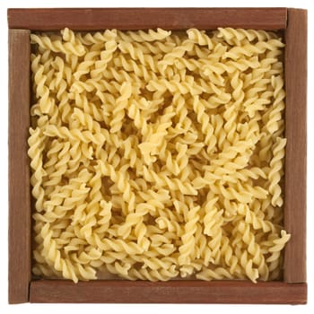 uncooked fusilli pasta in a rustic wooden box or frame isolated on white
