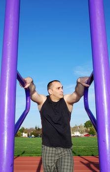 Male athlete  resting between exercises outdoors with blue sky and white clouds in the background.