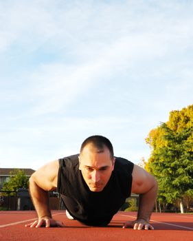 Male athlete doing push ups outdoors with blue sky and white clouds in the background.