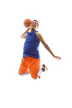 Young African American man playing basketball. It is a studio shot, and he is jumping in the air, about to slam dunk the basketball.