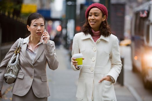 Two business women walking in the big city. One is on her cell phone.