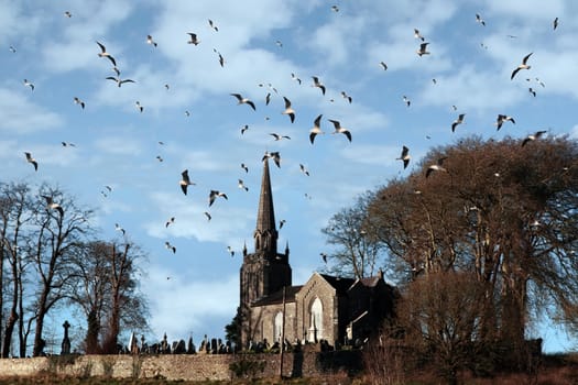 a church and graveyard on top of a hill with blue sky and a flock of birds