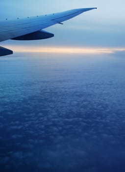 A soft landscape seen from the airplane, in the air, we can see the airplane's wing and the yellow, orange horizon with blue sky and many clouds.
