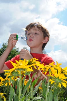 The boy in a red T-short blows soap bubbles on a background of the blue sky