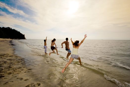 group of friends having fun jumping into the sea on sunset