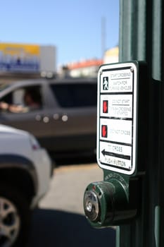 This shows an unexpected view of a traffic light button for pedestrian with some cars in the background. This is good for any traffic themes or something that has to do with controlling a situation.