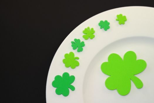 White plate on black background with green clover leafs.
