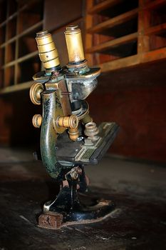 Aged microscope standing on an old wooden secretary.