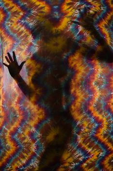 Woman silhouetted behind tye-dye fabric.