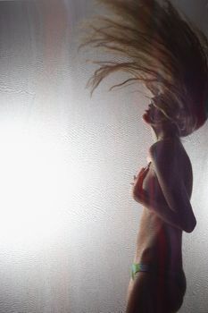 Sensual nude Caucasian woman behind sheer cloth flipping hair in to air.