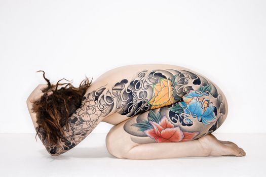 Nude caucasian woman with tattoos sitting on floor.