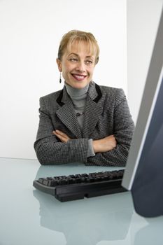 Caucasian woman looking at computer and smiling with arms crossed.