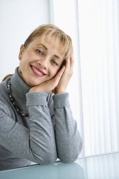 Caucasian woman with head resting on hand smiling at viewer.