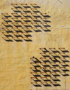 The wall of old house with strange iron construction which cast strict geometrical shadows.
