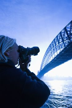 Caucasian teenage male photographing Sydney Harbour Bridge at dusk with view of Sydney Harbour, Australia.