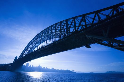 Sydney Harbour Bridge at dusk with view of distant skyline and harbour in Sydney, Australia.