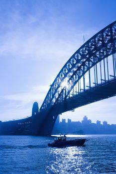 Boat under Sydney Harbour Bridge at dusk with view of distant skyline and harbour in Sydney, Australia.