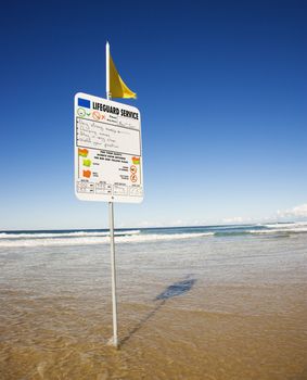 Sign and flag on beach in Surfers Paradise, Australia with lifeguard schedule.