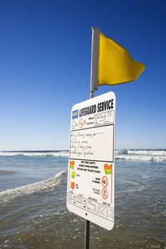 Sign and flag on beach in Surfers Paradise, Australia with lifeguard schedule.