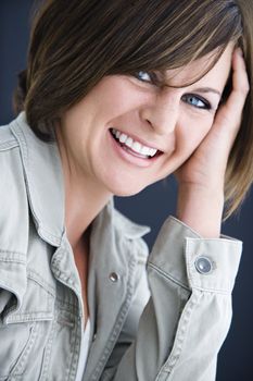 Caucasian mid adult brunette woman smiling at viewer resting head on hand.