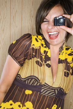 Caucasian mid adult brunette woman looking through miniature toy camera and making facial expression.