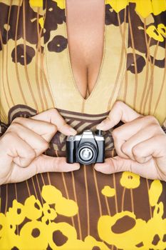 Torso of Caucasian woman holding miniature toy camera.