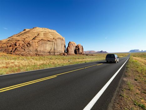 Sport utility vehicle on open highway in scenic desert landscape with butte land formation.