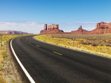 Curve in road in scenic desert road with mesa land formations and mountains.