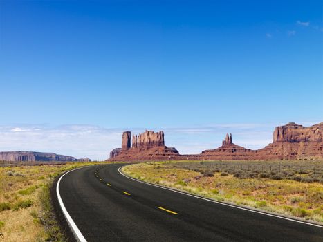 Scenic road in desert landscape with mesa and mountains.