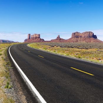 Curve in road in scenic desert road with mesa land formations and mountains.